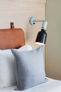 A minimalist bedroom with a gray cushion, a leather headboard, and a modern lamp on the wall.