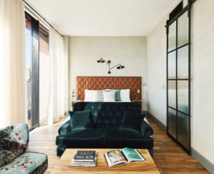 Modern bedroom featuring a green velvet sofa, a tufted leather headboard bed, and a wooden coffee table with books.
