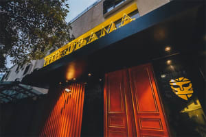 Modern metal storefront with a yellow neon sign reading "THE DRAMA"