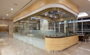 A modern restaurant with glass walls, marble flooring, and wooden accents.