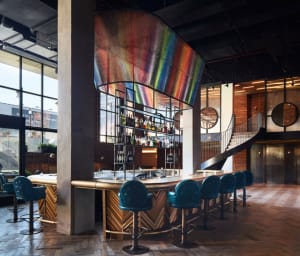Contemporary bar interior featuring modern furniture, metal accents, wood paneling, and a large, colorful suspended sculpture