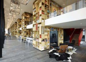 Modern, wooden bookshelves surrounded by comfortable seating areas in a large, open space with a circular light fixture hangi