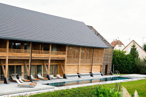 A modern residential exterior with a wooden facade and a pitched roof with a pool in the foreground.