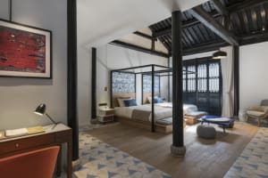 A modern bedroom featuring a desk, floor tiles with triangular patterns, and a large bed with a canopy frame.