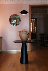 Modern entrance hall featuring a black cylindrical table with a round top, displaying a large, abstract ceramic vase with a h