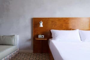 A minimalist bedroom featuring a wooden headboard with white bedding and a cozy corner sofa.