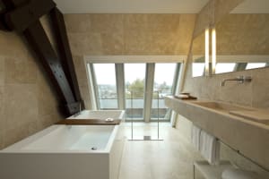 Modern bathroom with a white freestanding bathtub, a large marble sink vanity, and a large window providing a city view.