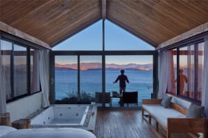 A modern bedroom featuring wood and glass elements with a view of the water.