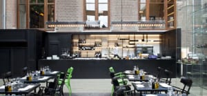 Interior design of a modern restaurant featuring a bar area with black countertops, wine bottles, and green chairs.
