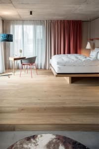 A modern bedroom featuring a wooden floor, a comfortable bed with a white mattress, and a desk area with a chair and a lamp.