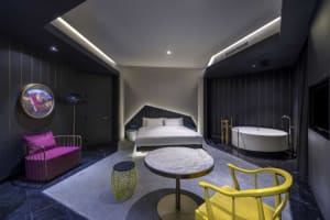 Modern minimalist bedroom with concrete walls, a white bed, and a yellow armchair.