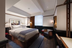 A modern bedroom with wooden furniture, white bedding, and a striped rug.