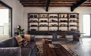 A modern industrial living room featuring wooden shelves, a gray sectional sofa, and a concrete floor.