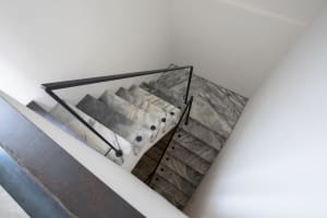 A modern staircase with marble steps and railings, viewed from above in a white-walled room.