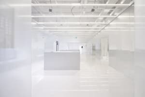 A long, white, minimalist office hallway with glass walls and overhead lighting.