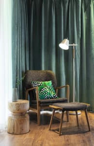 A modern living room with a comfortable chair and ottoman, featuring a palm leaf-patterned pillow and a floor lamp.