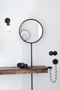 A minimalist bathroom featuring a wooden shelf with a hairdryer and a wall-mounted light bulb.
