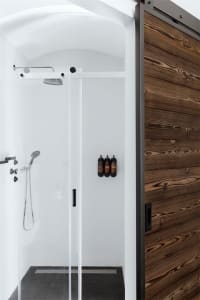 A modern minimalist bathroom features a wood-framed sliding door, a glass shower enclosure, and black tiles on the floor and 