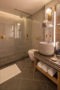 A modern minimalist bathroom with a stone sink, white toilet, and glass shower enclosure.