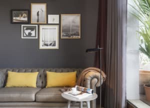 A living room with a gray sofa adorned with yellow pillows, situated against a dark gray wall, accompanied by a white side ta