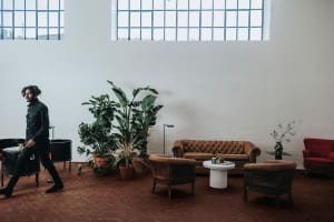 A spacious, industrial-style lobby with a brown brick floor, various indoor plants, and leather furniture.