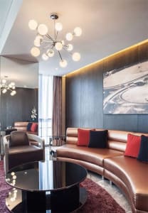 Modern living room featuring a curved leather sofa with red and black throw pillows, a black round coffee table, and a chande