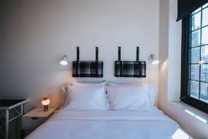 A modern minimalist bedroom featuring a black and white plaid upholstered headboard, white bedding, and a large window provid