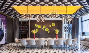 Modern restaurant dining room featuring concrete walls, glass ceiling accents, and a long dining table surrounded by white ch