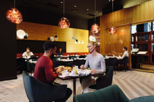 Modern restaurant interior with patrons seated at tables, contemporary lighting fixtures, and wooden walls.