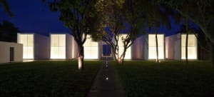A minimalist architectural building exterior at night, illuminated by interior lights.