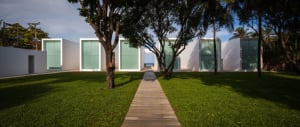 A minimalist modern house with white concrete walls and large glass windows surrounded by lush greenery and a neatly maintain
