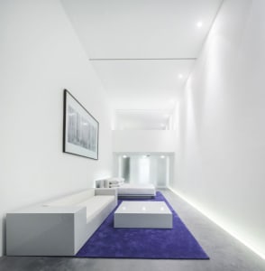A minimalist living room with white furniture and concrete flooring.