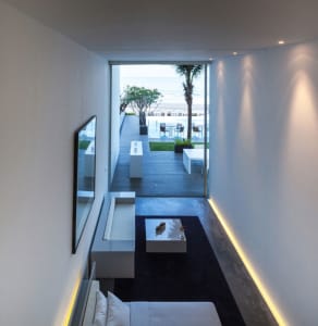 A modern residential interior featuring a concrete floor and minimalist decor, with a view of the beach through large windows