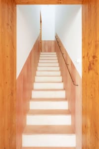 A staircase constructed with wooden steps and a concrete railing, surrounded by wooden walls.