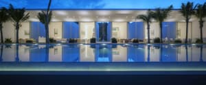 A modern residential exterior featuring a glass poolside with palm trees at dusk.