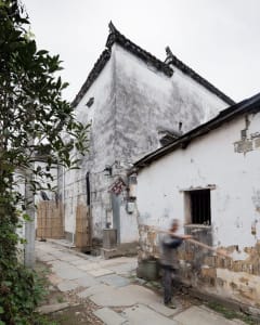 A narrow, urban street with ancient buildings made of concrete and wood.