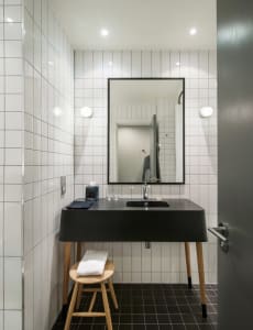 Industrial-style bathroom with white tiled walls, a concrete countertop, and a wooden stool.