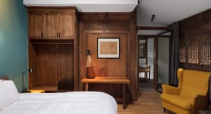 A minimalist bedroom with wooden furniture and decor, including a bed, desk, and a yellow chair.