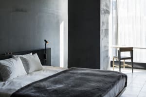 A minimalist bedroom with a concrete headboard, white bedding, and a dark grey blanket.