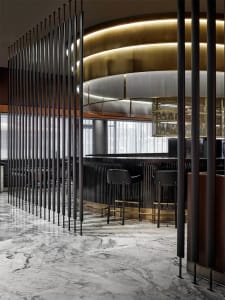 A modern restaurant bar with elegant marble flooring, glass partitions, and metallic accents.