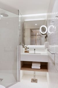 White-tiled bathroom with minimalist design, featuring a sink, shower, and towel storage.