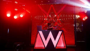 A DJ booth with a red light display and a large W logo in front of a red textured background.