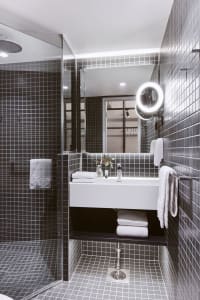 A minimalist black-tile bathroom features a walk-in shower and a white vanity.