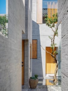 A minimalist grey concrete house with wood doors and a small tree in a pot.