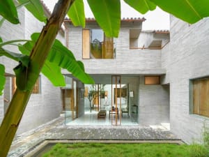 A modern residential house with concrete walls, glass doors, and greenery.