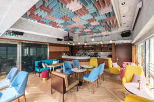 A stylish modern bar interior featuring colorful seating and a well-stocked bar counter.