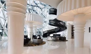 Modern hotel lobby featuring white marble flooring, black metal spiral staircase, and contemporary seating.