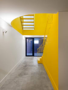 A minimalist interior design featuring a modern staircase with yellow metal railing and handrail, set against a white backgro