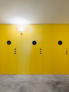 A row of bright yellow doors with dark circular holes and small black handles and locks, mounted on a concrete wall.
