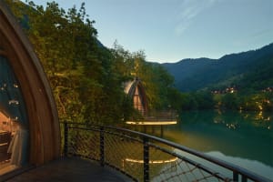 Hotel room with arched window overlooking tranquil water and mountains at dusk, built on stilts over calm lake.